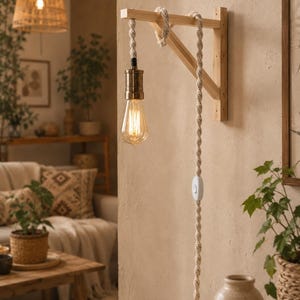 May include: A wooden wall light with a decorative rope cord and a vintage Edison bulb. The light fitting is made of light-coloured wood and has a simple, rustic design. The bulb is lit, casting a warm glow. The light is part of a home decor theme.