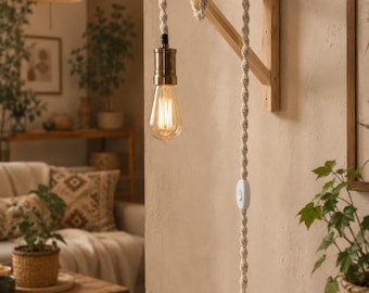 Op de afbeelding: Een houten wandlamp met een decoratief touwsnoer en een vintage Edison-lamp. De lamp is gemaakt van lichtgekleurd hout en heeft een eenvoudig, rustiek ontwerp. De lamp brandt en geeft een warme gloed. Onderdeel van een woondecoratiethema.