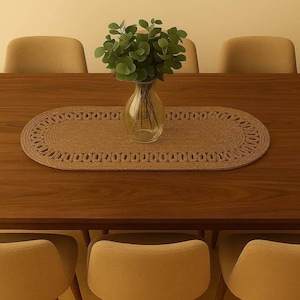 May include: A wooden dining table with a woven oval placemat and a clear glass vase holding green foliage. Beige chairs are positioned around the table. The placemat is made of a light brown material.