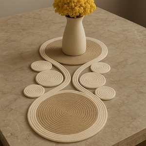 Peut inclure: Une décoration de table avec un vase beige contenant une composition florale jaune. Le vase repose sur un dessous de verre circulaire, avec un chemin de table assorti et des dessous de verre supplémentaires en spirale. La table est marron clair.