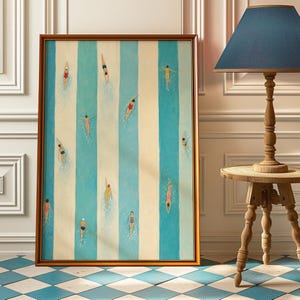 May include: A framed rectangular wall art print featuring a vertical striped pattern of alternating light blue and cream bands. The artwork depicts multiple small figures swimming in various poses within the blue stripes, wearing colourful swimsuits.