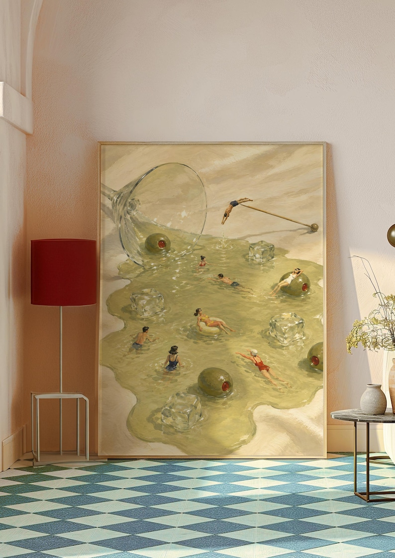 May include: A framed rectangular wall art print depicting a spilled martini glass on a light surface. The liquid forms a pool containing several people swimming, floating on an inflatable ring, and diving, alongside large green olives and ice cubes.