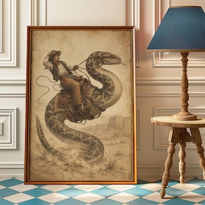 Könnte beinhalten: Ein gerahmter Kunstdruck mit einer sepiafarbenen Illustration eines Cowboys mit Hut, Weste und Chaps, der auf einer riesigen Klapperschlange durch eine Wüstenlandschaft reitet. Das Bild zeigt die Figur, die ein Lasso hält, während sie auf der Schlange sitzt.