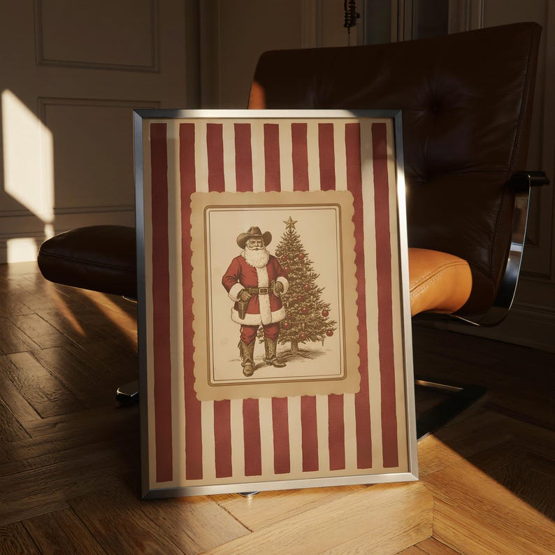 May include: Framed artwork featuring a cowboy Santa Claus illustration. The image shows Santa in a red coat and cowboy hat, standing next to a Christmas tree. The frame has a red and cream striped pattern.