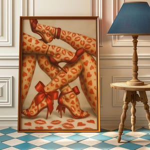May include: Framed artwork featuring legs adorned with red heart and lip patterns. The legs wear red high heels, one pair with large bows. The artwork is in a gold frame, set against a white wall and a blue and white checkered floor.