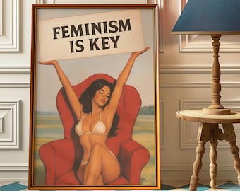 May include: Framed artwork featuring a seated figure in a red chair, holding a sign that reads "FEMINISM IS KEY." The figure is wearing a white bikini. The artwork is in a gold frame.