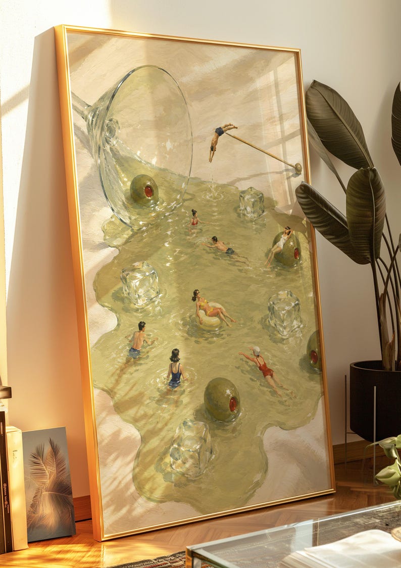 May include: A framed rectangular wall art print featuring a surreal illustration of a spilled martini glass. The liquid forms a pool containing small figures swimming, diving, and floating on ice cubes, with large green olives scattered throughout.