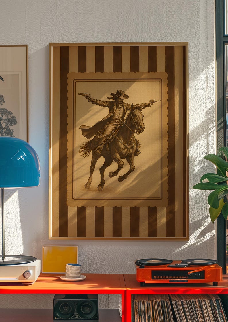 May include: Framed sepia-toned print of a cowboy on horseback, arms outstretched, holding two pistols. The artwork is set against a striped background and framed in a wooden border. The image evokes a vintage Western theme.