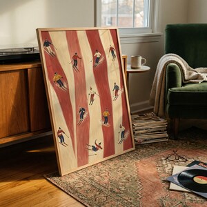 May include: A rectangular framed wall art print featuring a vertical pattern of alternating cream and terracotta red stripes. The artwork depicts multiple small figures of skiers in various colorful winter outfits skiing down the slopes.