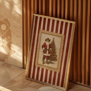 May include: A framed Christmas print featuring Santa Claus in a cowboy hat and red suit, standing next to a decorated Christmas tree. The frame has a gold finish and the background has red and white stripes.