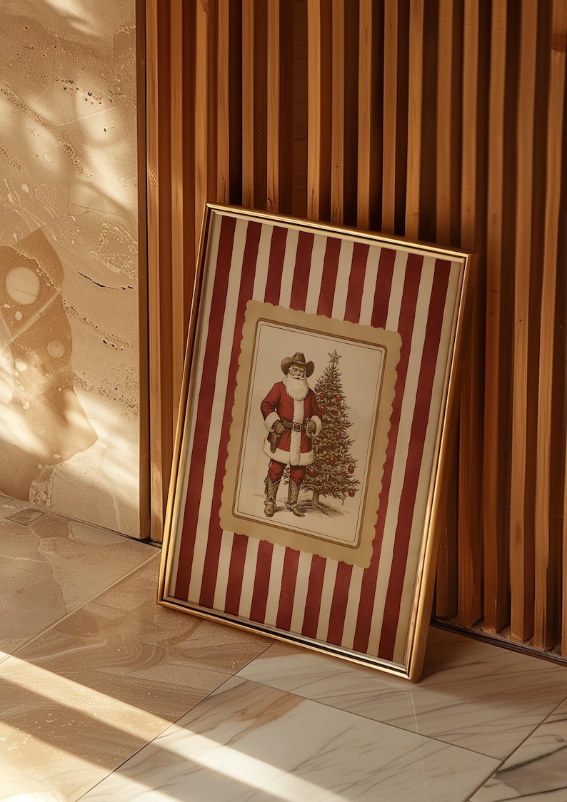 May include: A framed Christmas print featuring Santa Claus in a cowboy hat and red suit, standing next to a decorated Christmas tree. The frame has a gold finish and the background has red and white stripes.