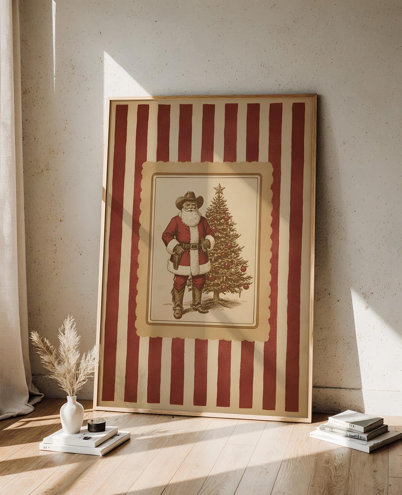 May include: Framed print featuring a cowboy Santa Claus standing next to a Christmas tree. The print has a red and cream striped background. The Santa illustration is in a cream-colored frame with a scalloped edge.