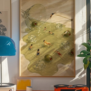 May include: A framed wall art print depicting a spilled martini glass on a sandy surface, with people swimming in the puddle of liquid alongside large green olives and translucent ice cubes, while one person dives from a cocktail pick.