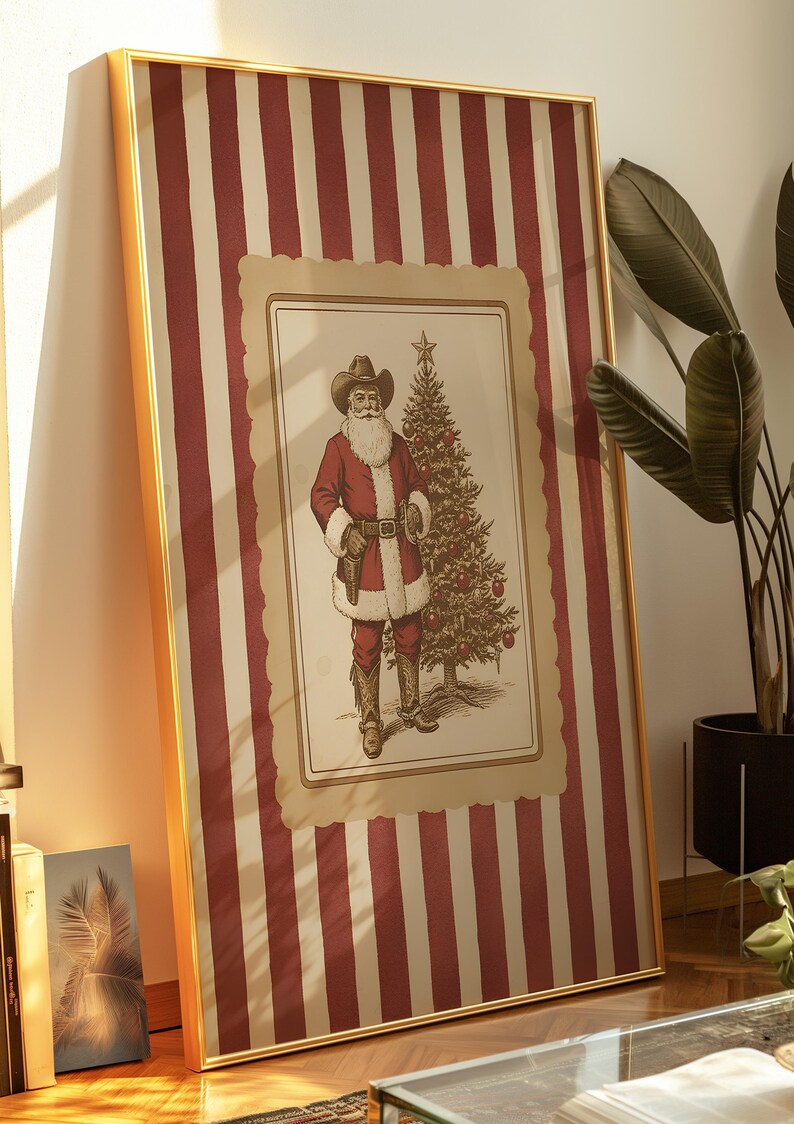May include: Framed Christmas art featuring a cowboy Santa Claus with a white beard, wearing a cowboy hat and red suit, standing next to a decorated Christmas tree. The background has red and white vertical stripes. The frame is gold.