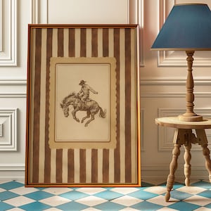 May include: A framed sepia-toned illustration of a cowboy riding a bucking horse. The artwork is set against a backdrop of brown and cream vertical stripes, framed in a gold-coloured border. The artwork is displayed on a blue and white checkered floor.