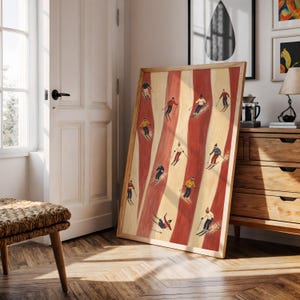 May include: A rectangular framed wall art print featuring a repeating pattern of vertical red and cream stripes with small illustrations of skiers in various colorful winter outfits, including hats, jackets, and pants, actively skiing down the slopes.