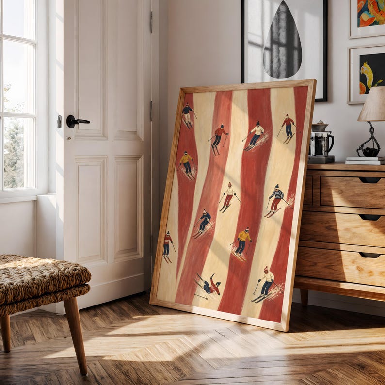 May include: A rectangular framed wall art print featuring a repeating pattern of vertical red and cream stripes with small illustrations of skiers in various colorful winter outfits, including hats, jackets, and pants, actively skiing down the slopes.