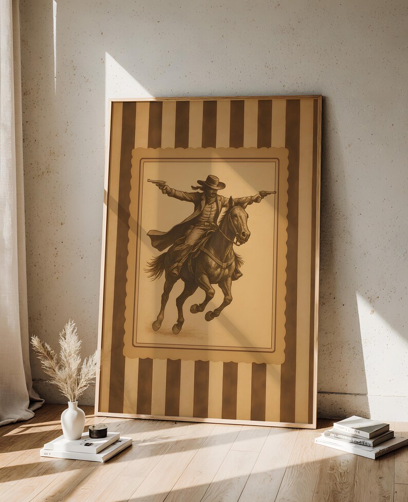 May include: Framed sepia-toned print of a cowboy on horseback, arms outstretched, holding two pistols. The artwork is set against a tan background with a decorative border and a striped frame. The image evokes a classic Western theme.