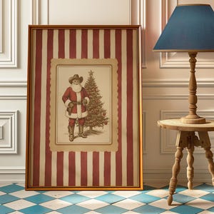May include: Framed artwork featuring a cowboy Santa Claus illustration. The artwork is set against a red and white striped background, framed in gold. A Christmas tree is next to Santa. The artwork is displayed near a wooden lamp and table.
