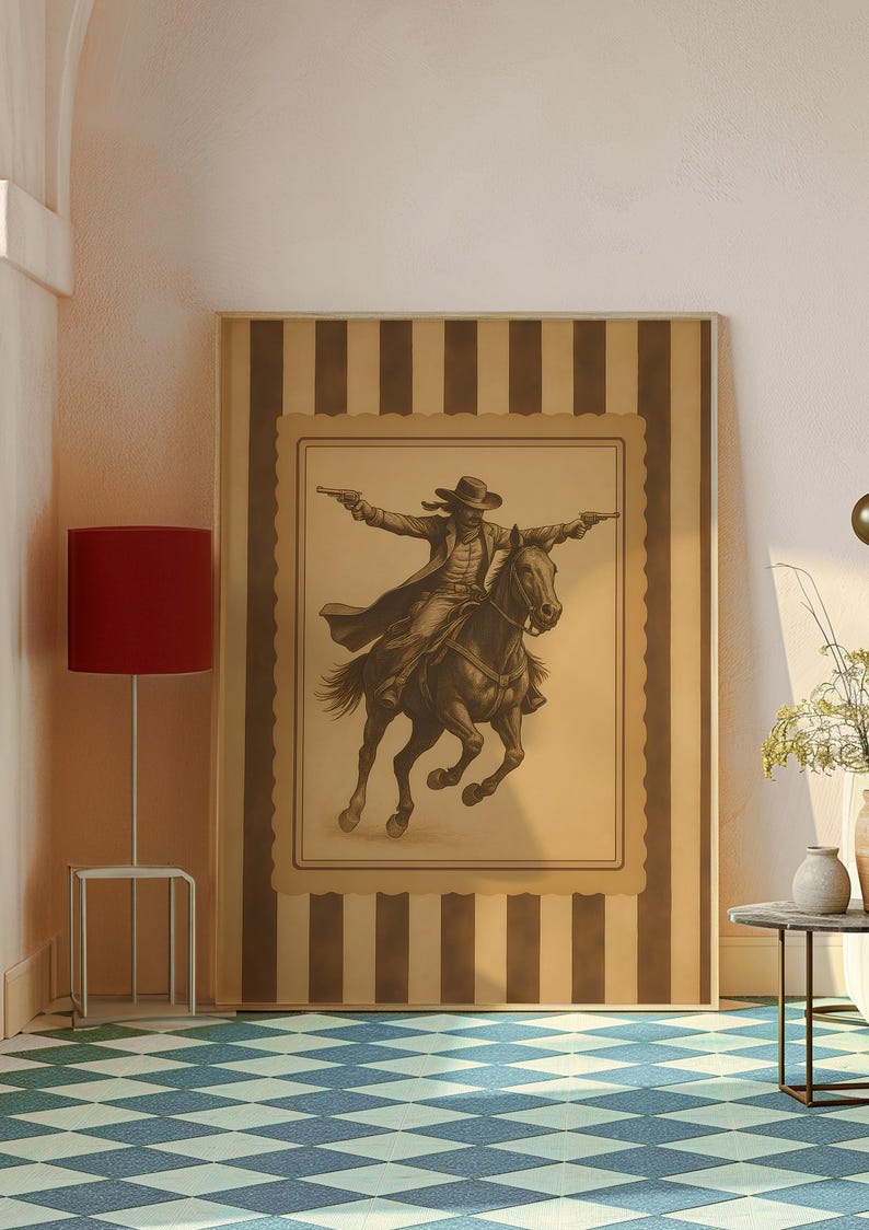 May include: A framed sepia-toned print of a cowboy on horseback, arms outstretched, holding two pistols. The artwork is set against a striped background with a decorative border. The print is displayed in a room with a red lamp and a patterned floor.