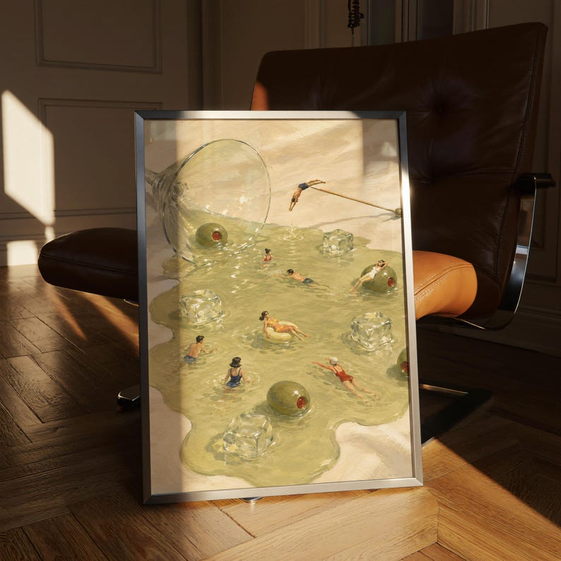 May include: A framed art print depicting a spilled martini glass on a light surface, with the liquid forming a pool containing ice cubes, large green olives, and several small figures swimming or lounging on inflatables within the drink.