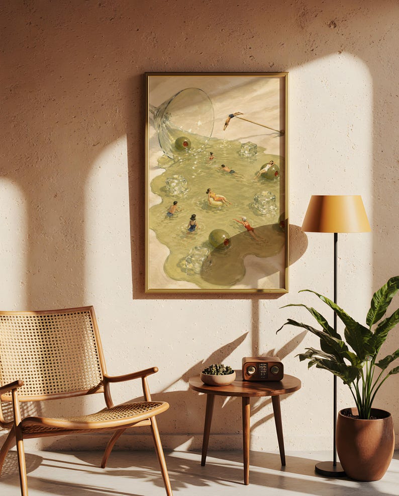 May include: A framed wall art print depicting a spilled martini glass on a sandy surface, with the liquid forming a pool where small figures swim among ice cubes and green olives. The scene features a light green color palette and surreal imagery.