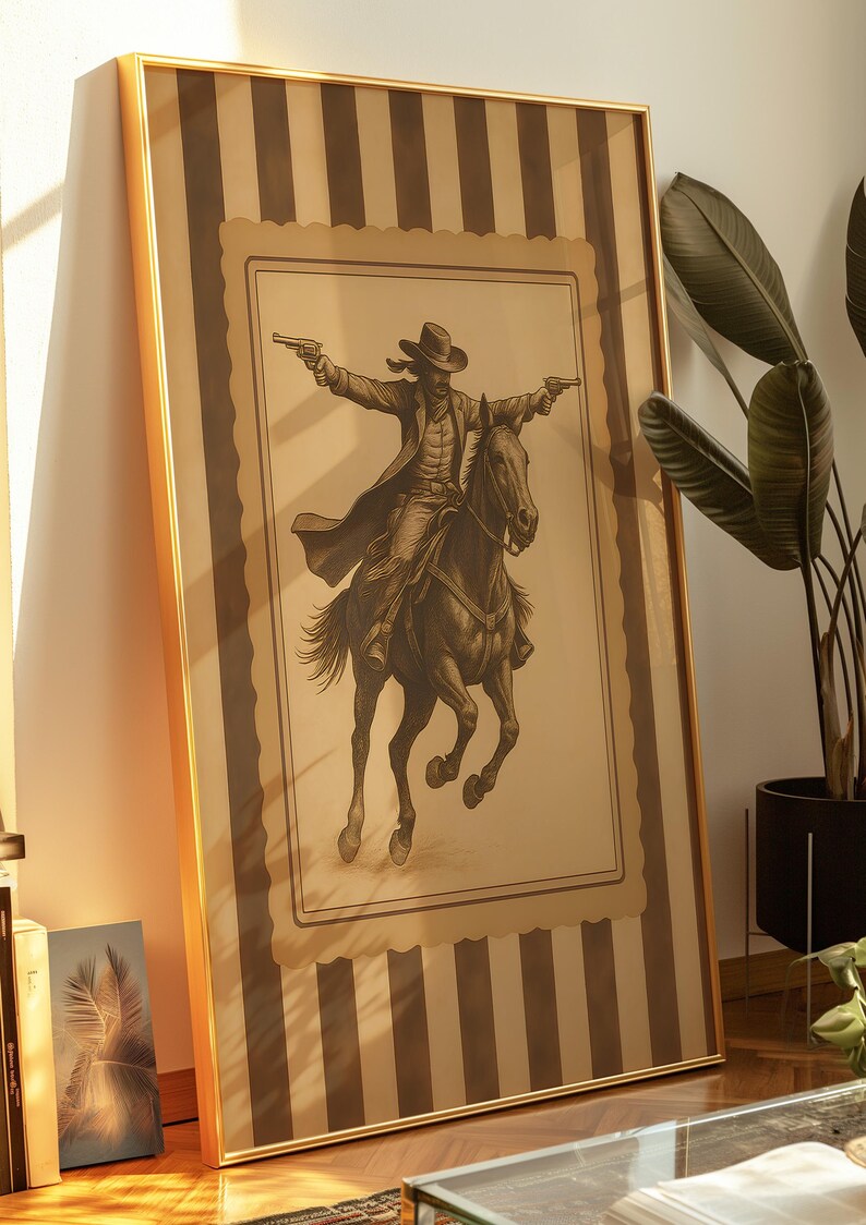 May include: Framed artwork featuring a sepia-toned illustration of a cowboy on horseback, holding two pistols. The artwork is in a gold frame and has a striped background.