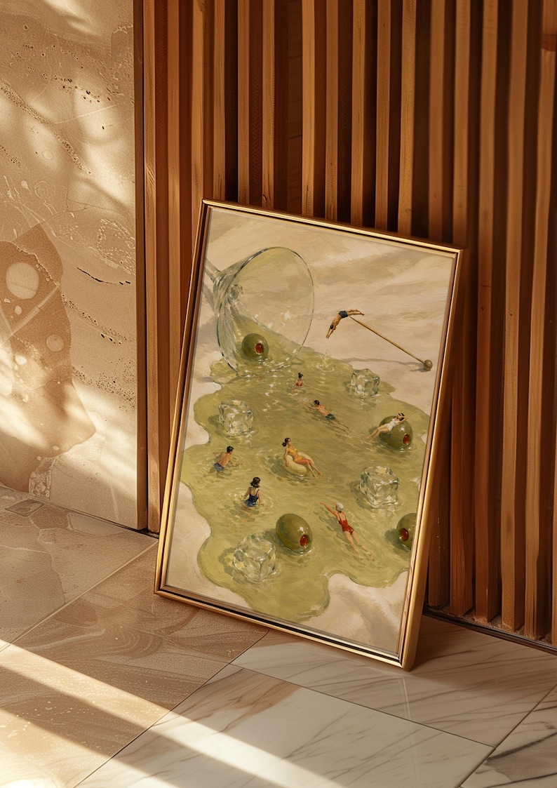 May include: A framed rectangular art print featuring a surreal illustration of a spilled martini glass. The liquid forms a pool containing small figures swimming, floating on green olives, and ice cubes, with a cocktail pick resting nearby.