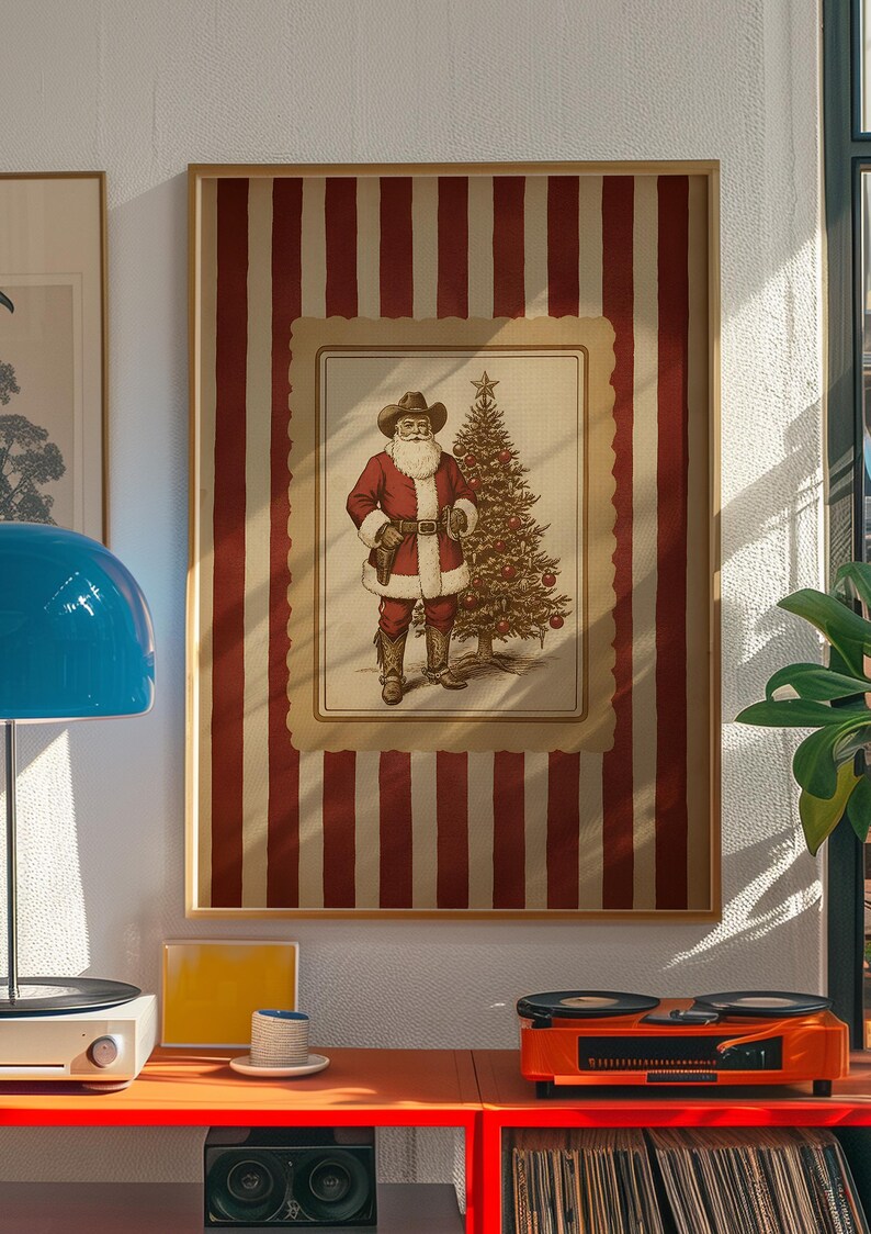 May include: Framed print featuring a cowboy Santa Claus with a Christmas tree. The artwork is set against a red and white striped background. The image is in a wooden frame and is displayed on a white wall.