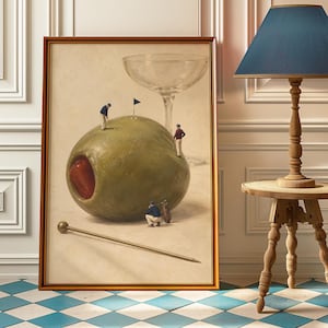 May include: A framed rectangular wall art print depicting a large green olive with a red pimento centre. Three miniature figures dressed in golf attire are positioned on and around the olive, which serves as a golf course with a flag and a martini glass.