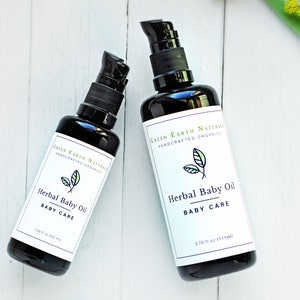 May include: Two black bottles of Herbal Baby Oil with black pump dispensers. Each bottle has a white label with the text "Green Earth Naturals Handcrafted Organics" and "Herbal Baby Oil BABY CARE". One bottle is 1.59 fl oz (50 ml), the other is 3.75 fl oz (111 ml).