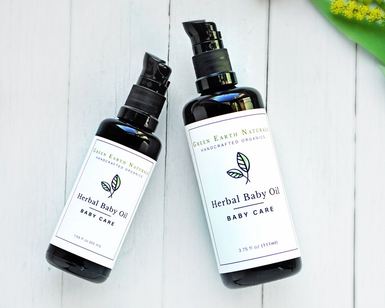 May include: Two black bottles of Herbal Baby Oil with black pump dispensers. Each bottle has a white label with the text "Green Earth Naturals Handcrafted Organics" and "Herbal Baby Oil BABY CARE". One bottle is 1.59 fl oz (50 ml), the other is 3.75 fl oz (111 ml).