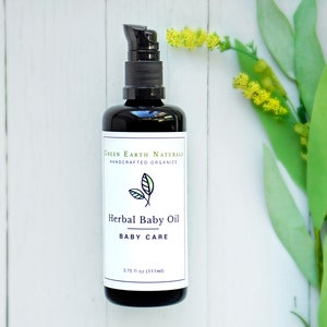 May include: A black bottle of Herbal Baby Oil with a pump dispenser. The label reads "Green Earth Naturals, Handcrafted Organics" and "Herbal Baby Oil, Baby Care." The bottle contains 3.75 fl oz (111ml). Green and yellow flowers are in the background.