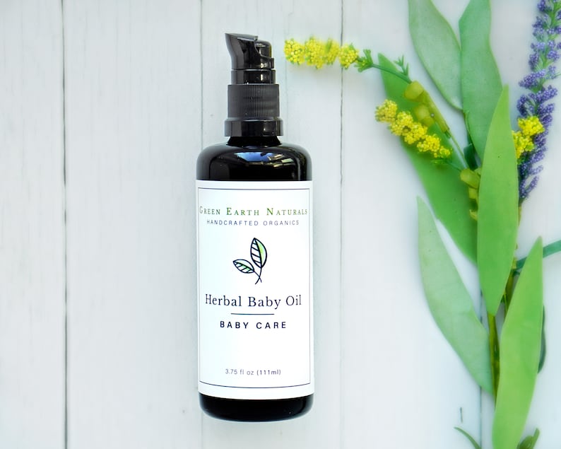 May include: A black bottle of Herbal Baby Oil with a pump dispenser. The label reads "Green Earth Naturals, Handcrafted Organics" and "Herbal Baby Oil, Baby Care." The bottle contains 3.75 fl oz (111ml). Green and yellow flowers are in the background.