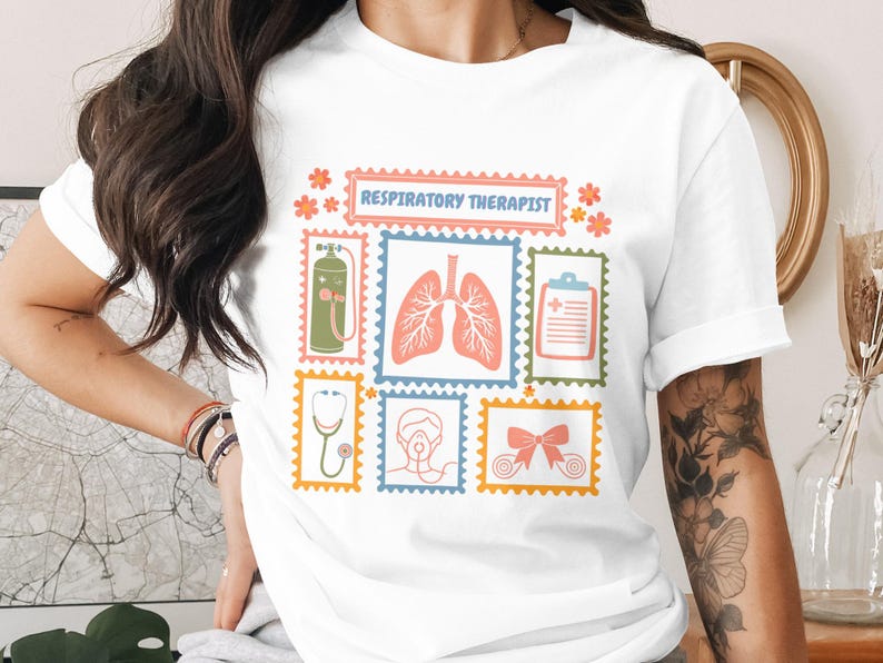 May include: White t-shirt featuring a colorful design with the text "RESPIRATORY THERAPIST". The design includes illustrations of lungs, a stethoscope, an oxygen tank, and other medical-related images. The shirt is made of a soft material.