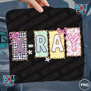 May include: A black square featuring the word "X-RAY" in decorative letters. The letters are in various patterns, including gingham, stripes, and floral designs, with pink bows and daisy accents.