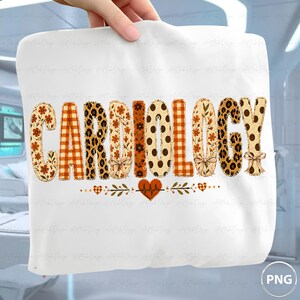May include: A white t-shirt featuring the word CARDIOLOGY in large, patterned letters. The letters incorporate floral, plaid, leopard print, and polka dot designs in orange, brown, and tan. A small heart with an EKG line sits below the text.