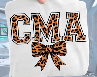 May include: White sweatshirt with the letters "CMA" in a leopard print design, outlined in black. A matching leopard print bow is centered below the letters. The sweatshirt is held up by a hand.