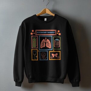 May include: Black sweatshirt with a colorful graphic design featuring medical-themed postage stamps. The stamps include images of lungs, a stethoscope, and the text "RESPIRATORY THERAPIST". The design is in shades of blue, orange, green, and yellow.