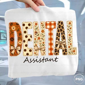 Könnte beinhalten: Ein weißes T-Shirt mit dem Text DENTAL ASSISTANT. Das Wort DENTAL ist in großen, dekorativen Buchstaben mit verschiedenen Mustern dargestellt, darunter orangefarbene Blumen, braune Punkte, orangefarbenes Vichy-Karo und Leopardenmuster, verziert mit kleinen Schleifen.