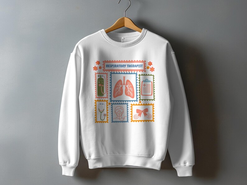 May include: White sweatshirt featuring a colorful design with the text "RESPIRATORY THERAPIST". The design includes illustrations of medical equipment and the lungs, set within postage stamp-like frames. The sweatshirt is hanging on a wooden hanger.