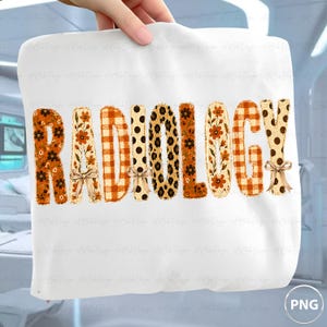 May include: A white t-shirt featuring the word RADIOLOGY in large, stylized letters. Each letter has a unique pattern including orange flowers, orange and white gingham, black polka dots, and leopard print, with small tan bows on some letters.