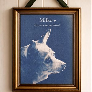 May include: Framed portrait of a dog named Milka, with the text "Forever in my heart." The dog's profile is in white against a blue background. The frame is gold, and the picture hangs from a green ribbon.