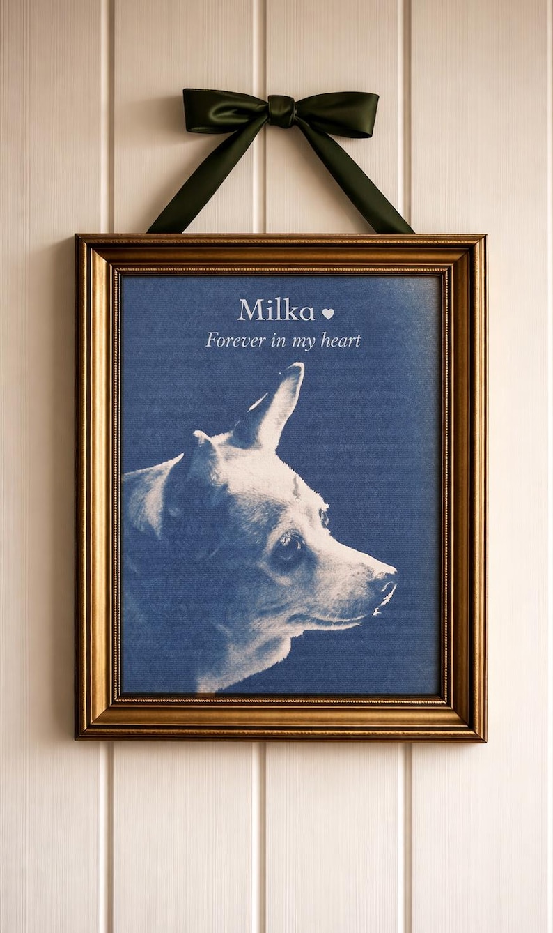 May include: Framed portrait of a dog named Milka, with the text "Forever in my heart." The dog's profile is in white against a blue background. The frame is gold, and the picture hangs from a green ribbon.