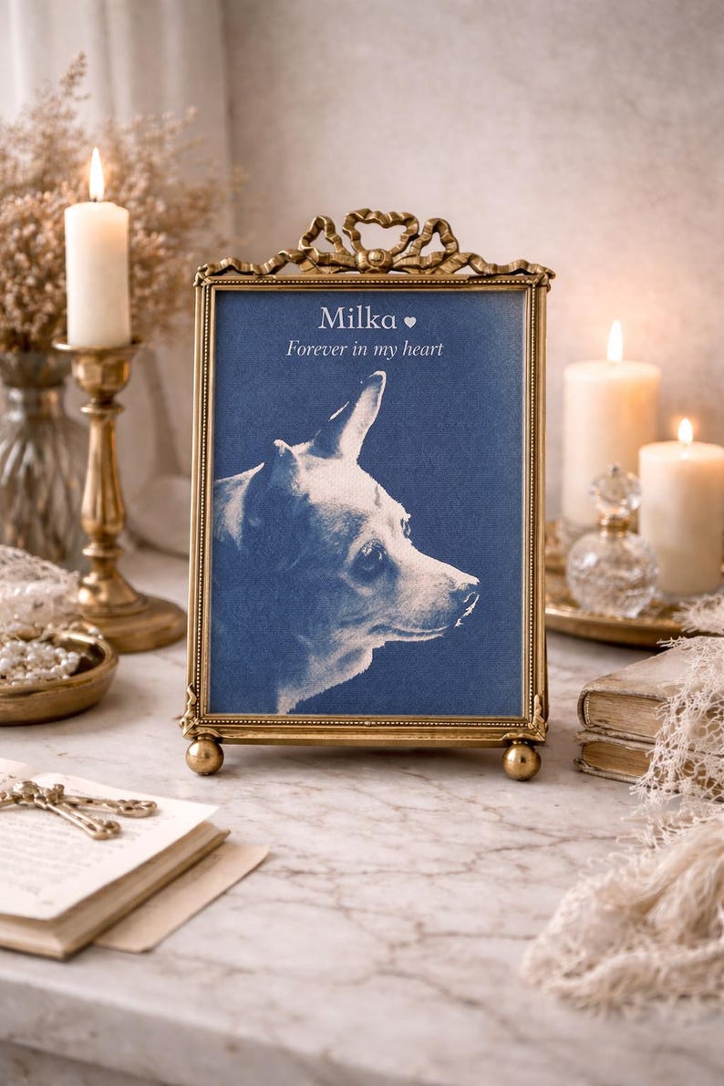 May include: A framed portrait of a dog named Milka, with the text "Forever in my heart." The portrait is in a gold-colored ornate frame with a blue background. The image is set on a marble surface with candles and decorative items.