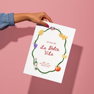 Op de afbeelding: Een witte print met de tekst "La Dolce Vita" omringd door een groene wijnstok met illustraties van voedsel zoals een citroen, druiven en een tomaat. Er is ook een fles wijn afgebeeld.
