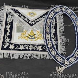 May include: A Masonic apron and collar set. The apron is white with a navy blue border, intricate embroidery, and fringe. The collar is navy blue with silver-colored embellishments and a chain.