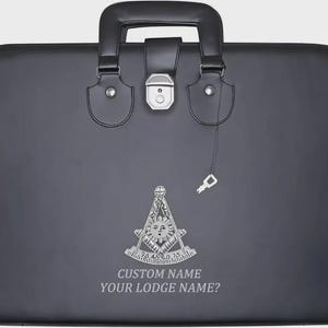 May include: A black briefcase with a handle, clasp, and key. The front features a silver emblem with the text "CUSTOM NAME YOUR LODGE NAME?"