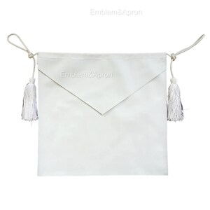May include: A white apron with a triangular flap and two white tassels. The apron has the text "Emblem&Apron" printed on it. The apron is made of a smooth, opaque material and has a rope tie.