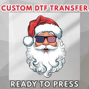 May include: A custom DTF transfer featuring a graphic illustration of Santa Claus wearing sunglasses with an American flag pattern. The text CUSTOM DTF TRANSFER appears at the top and READY TO PRESS is at the bottom of the white square design.